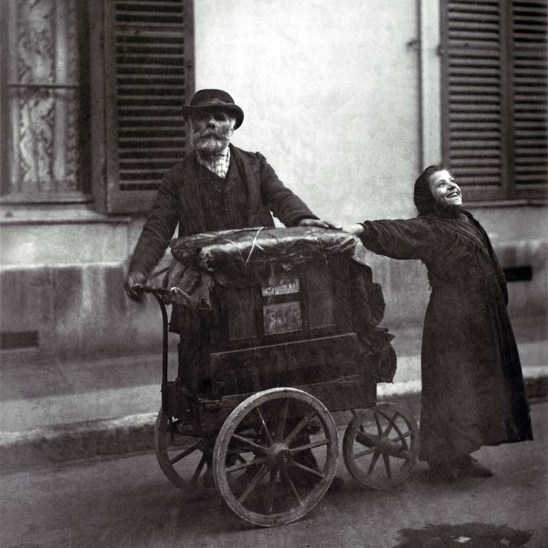 A black and white photo of an older man and a young girl standing with a street organ.
