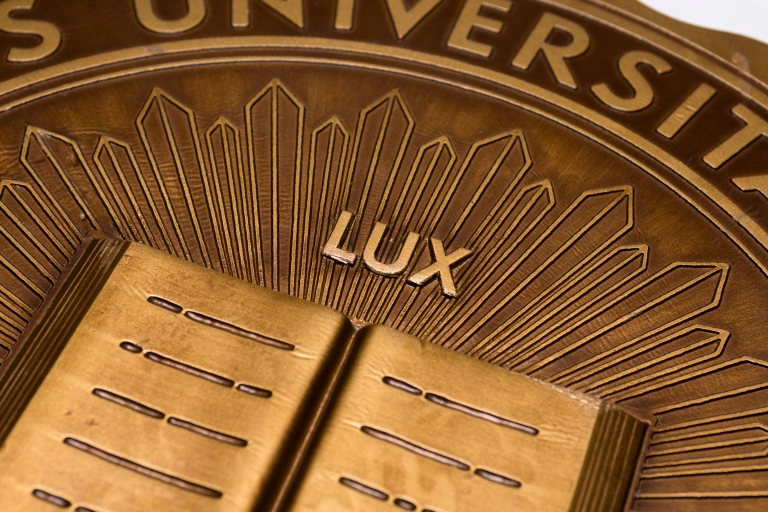 Close up of "Lux" carved in brass above a carving of an open book.